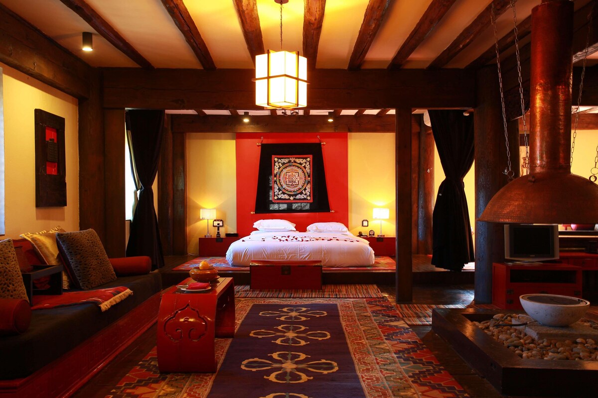 A room with a large bed, a red sofa, a wooden ceiling, and a stone fireplace.