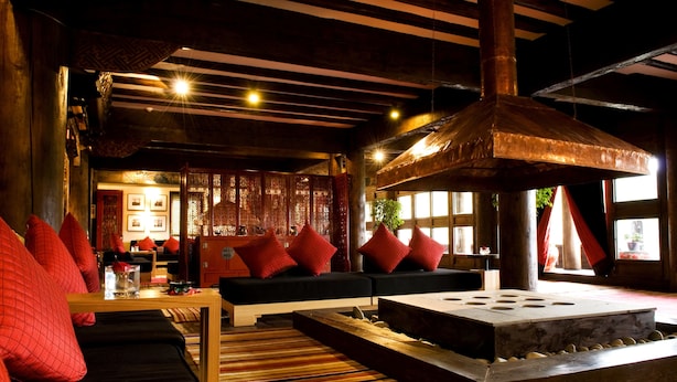 A modern interior with a black sofa, red cushions, a wooden coffee table, and a stone fireplace. - Banyan Tree Ringha (Deqin)