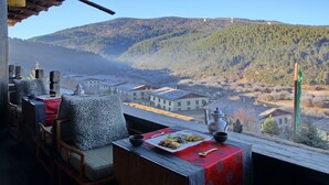 A dining area with a table set for two, overlooking a valley with houses and mountains. - Banyan Tree Ringha (Deqin)