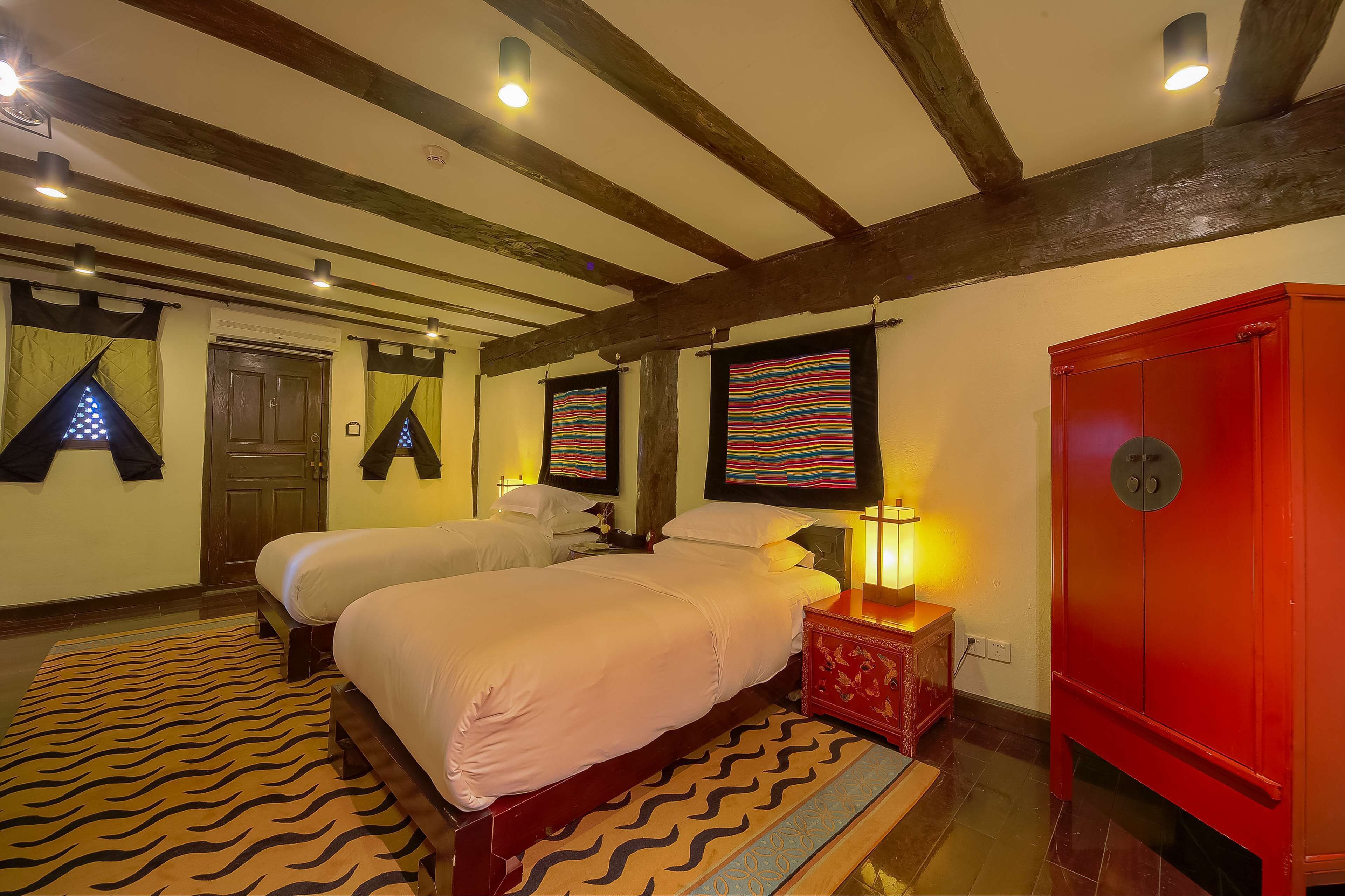 A bedroom with two beds, a red wardrobe, and a patterned rug.