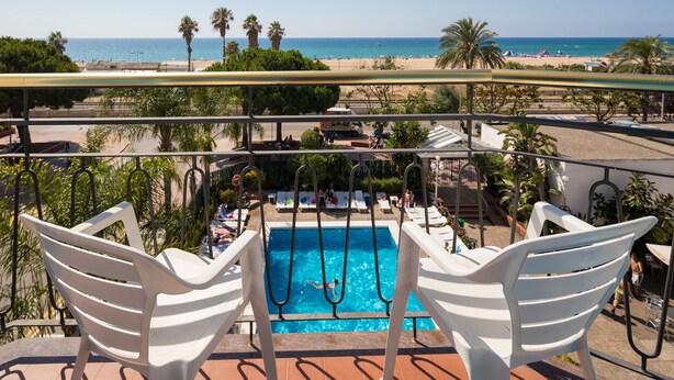 A balcony with a view of a pool, beach, and palm trees. - htop Planamar (Malgrat de Mar)