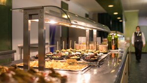 A buffet with various food items and a service staff member in the background. - htop Planamar (Malgrat de Mar)