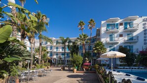 A hotel with a pool, outdoor seating, palm trees, and a clear blue sky. - htop Planamar (Malgrat de Mar)