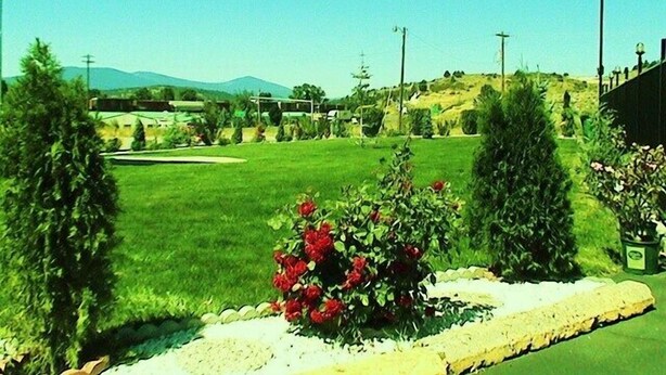 A well-maintained lawn with a flower bed in the foreground, a clear sky, and distant hills.