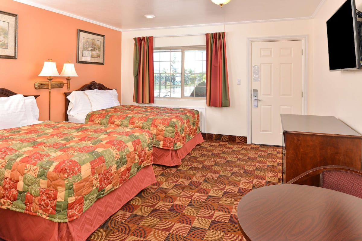 A hotel room with two beds, a desk, a chair, a window with curtains, and a television on the wall.