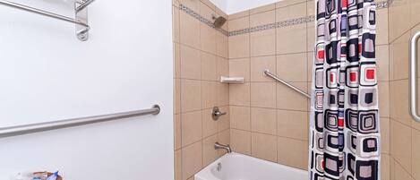A bathroom with a bathtub, a shower, a grab bar, a towel rack, and a basket on the toilet.
