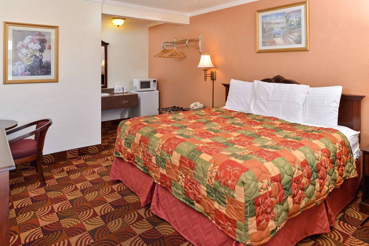 A hotel room with a large bed, a desk, a chair, a microwave, a telephone, and a wall-mounted lamp.