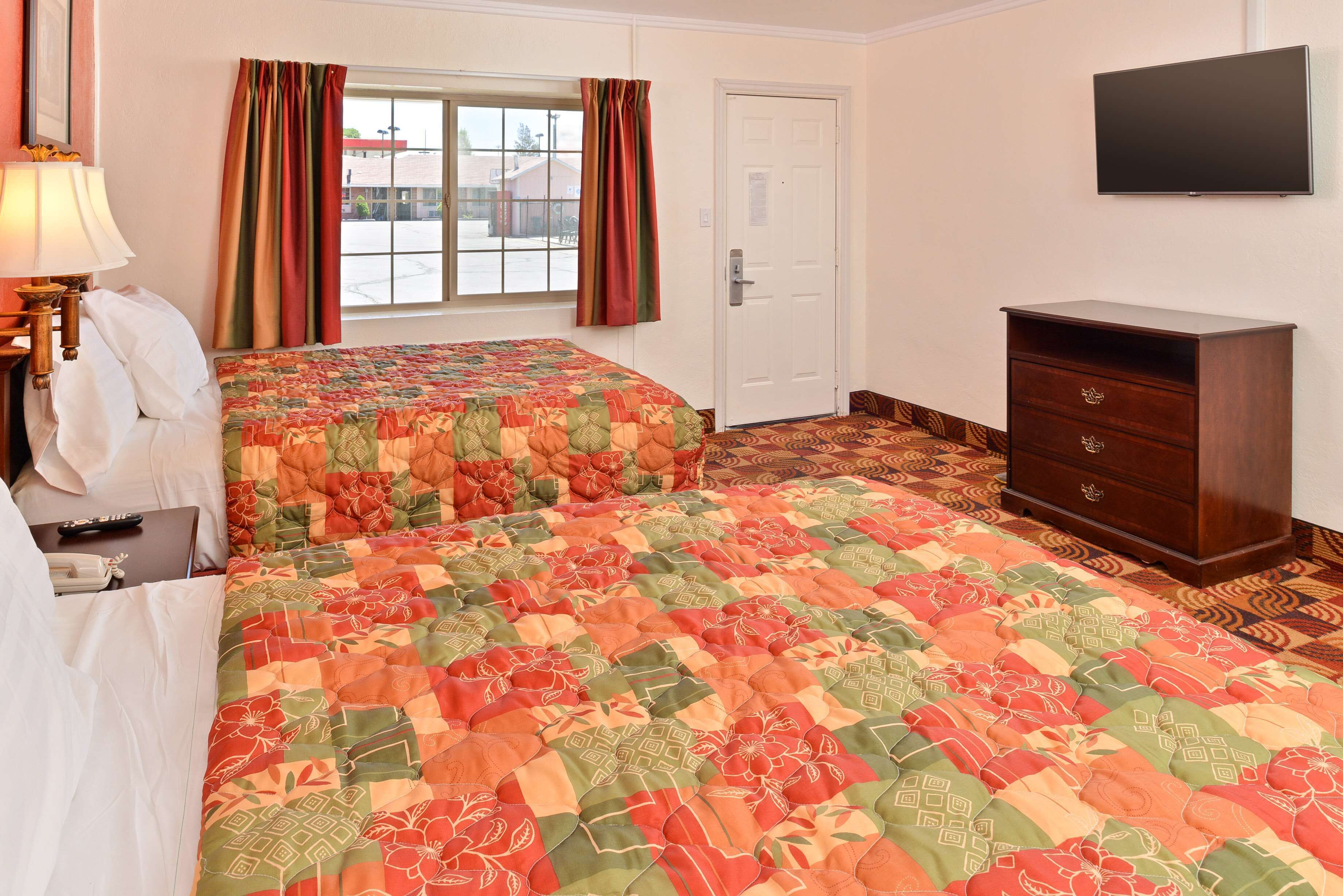 A hotel room with two beds, a dresser, a TV, and a window with curtains.