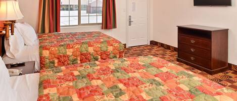 A hotel room with two beds, a dresser, a TV, and a window with curtains.