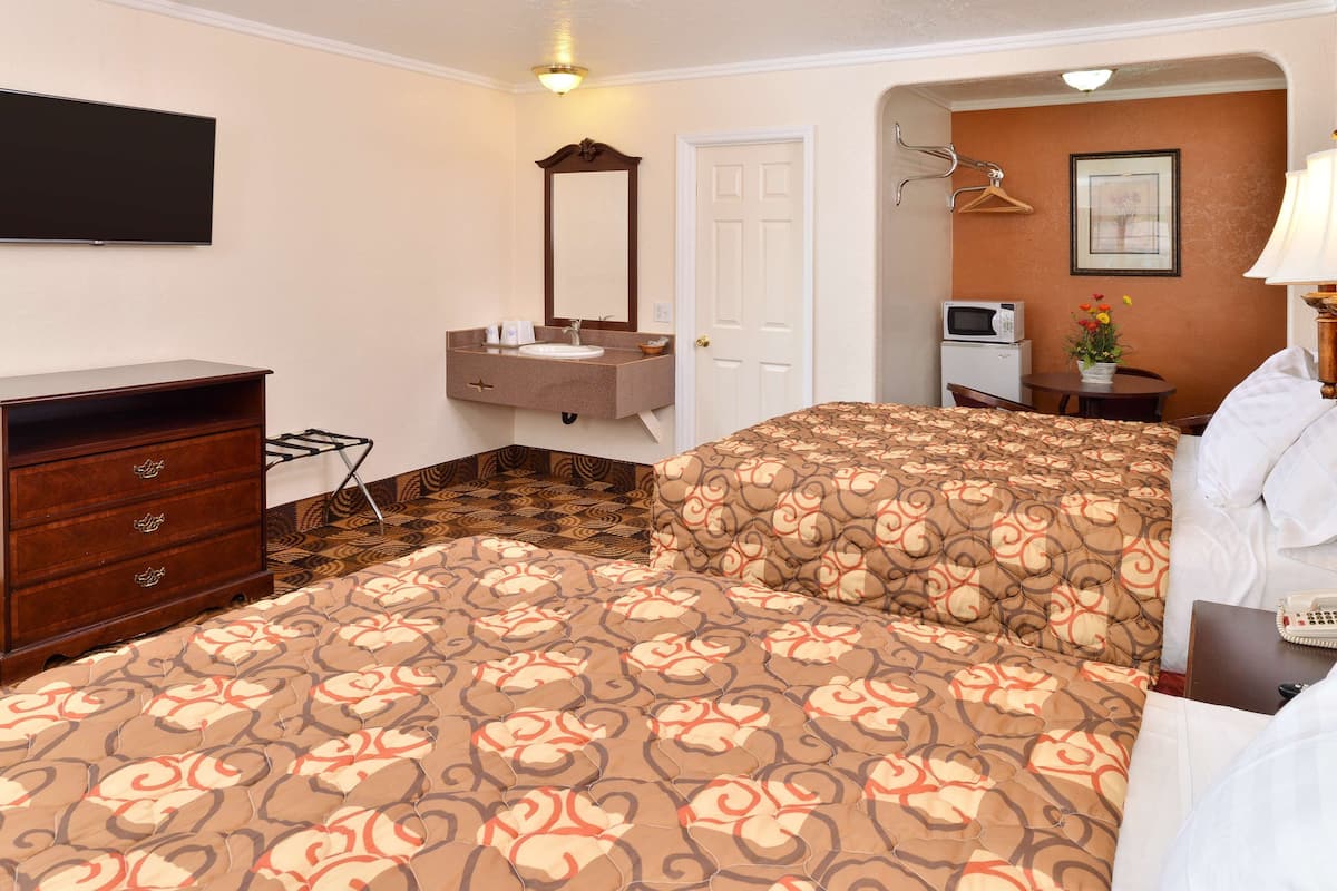 A hotel room with a bed, a dresser, a vanity with a mirror, a television, a microwave, and a small table with a vase of flowers.