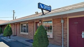 A single-story building with a red door and a sign indicating an office. There are two small trees in front of the building.