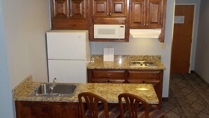 A compact kitchen with wooden cabinets, a built-in microwave, a refrigerator, a granite countertop, and a sink. - SureStay Plus Hotel by Best Western Warner Robins AFB (Warner Robins)