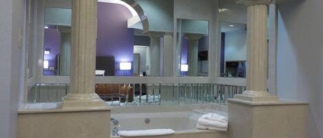 Un baño moderno con una bañera grande, un espejo y vistas al vestíbulo del hotel.