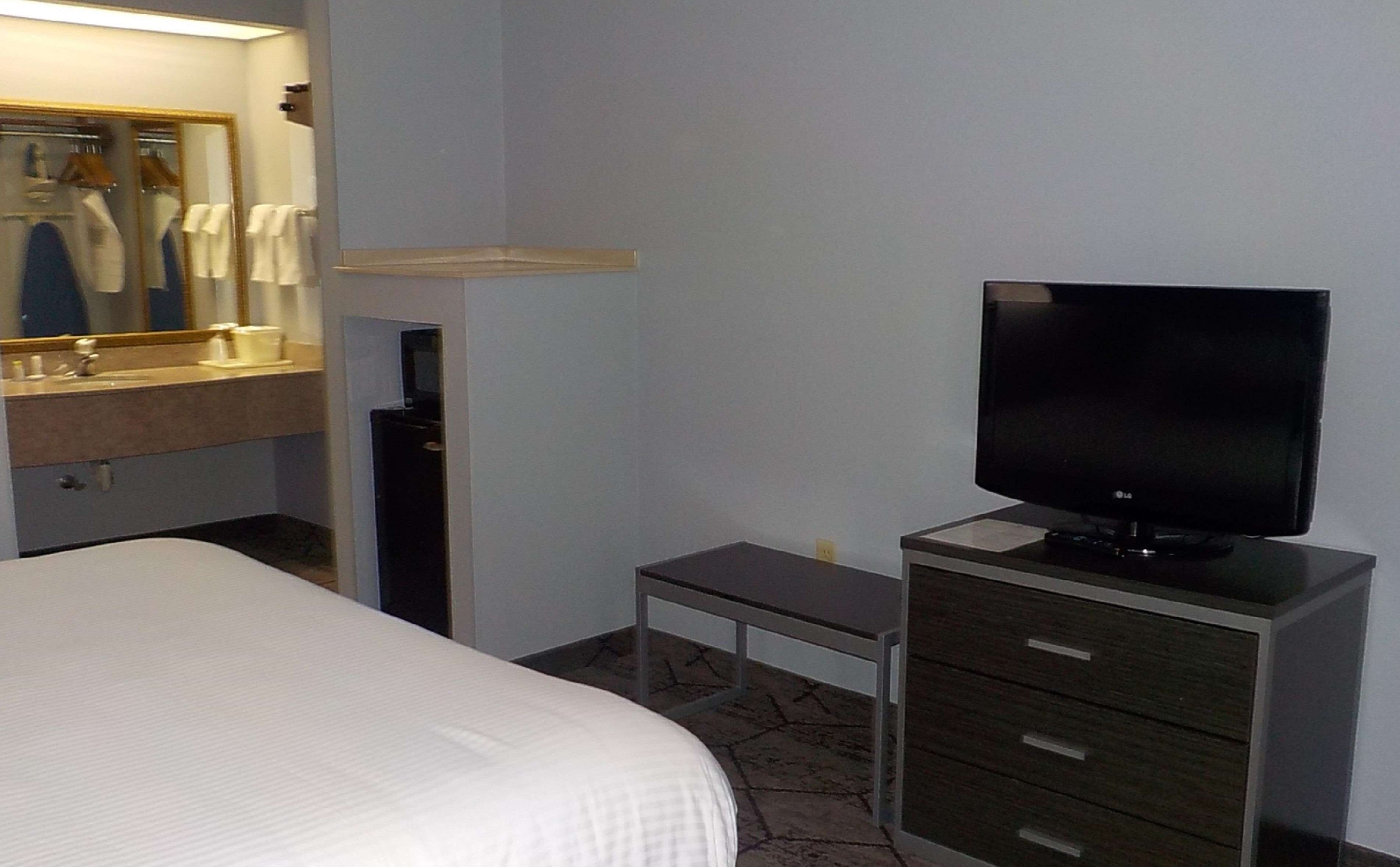 A hotel room with a bed, a TV on a stand, a mirror, and a small table.