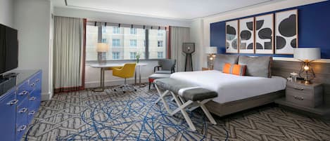 Ein Hotelzimmer mit Bett, Schreibtisch, Stuhl, Fernseher und einem großen Fenster.