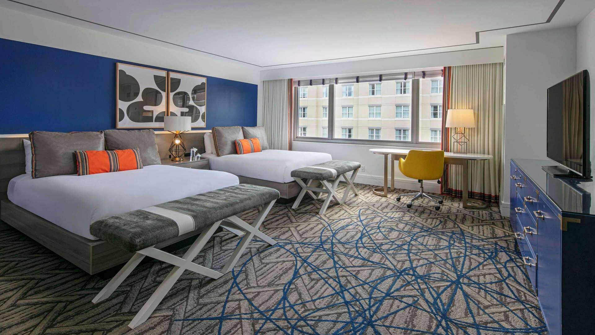 Een hotelkamer met twee bedden, een bureau, een stoel en een televisie.
