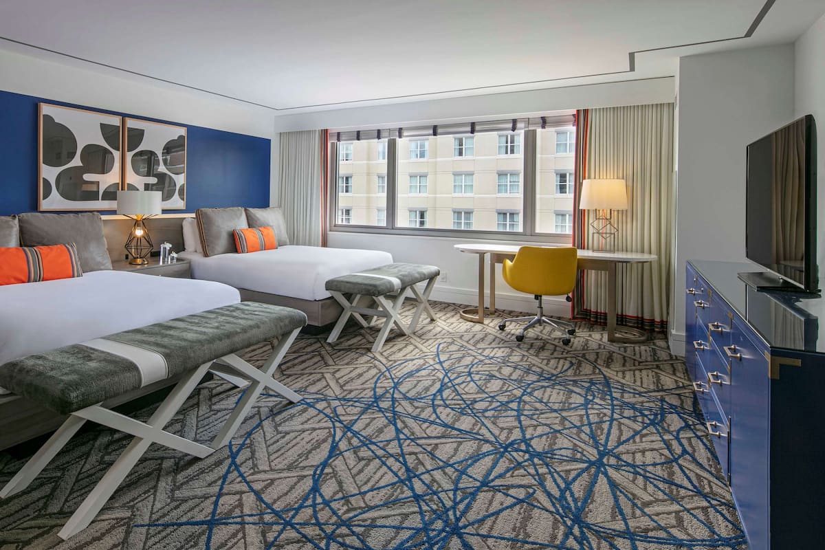 A hotel room with a large bed, a desk, a chair, and a TV.