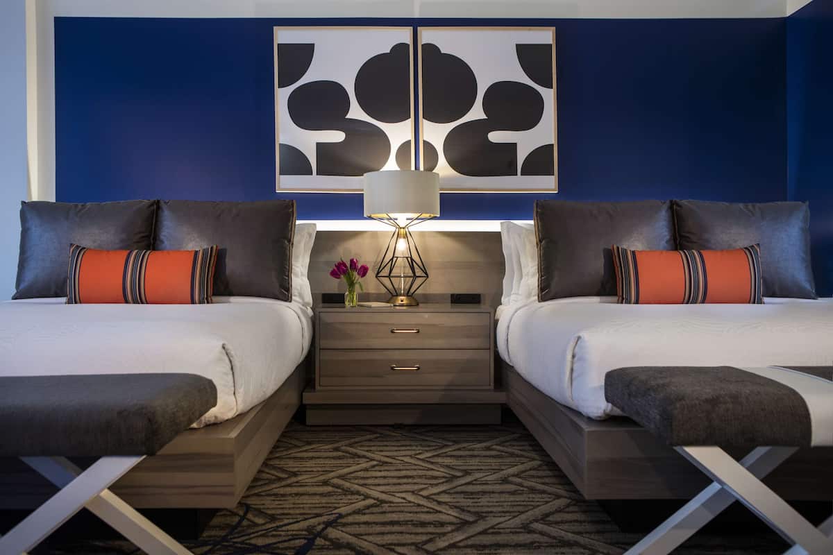 A hotel room with two beds, a nightstand with a lamp, and a decorative wall piece.