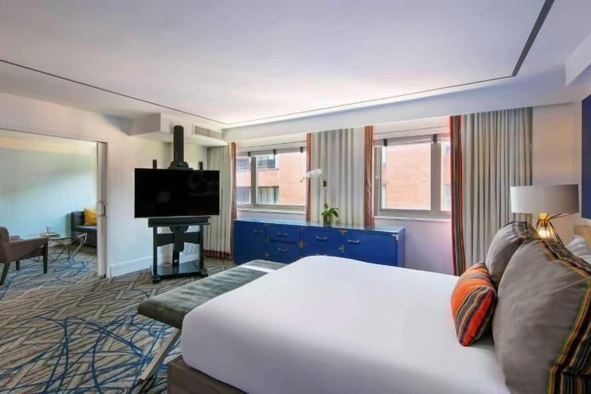 A hotel room with a bed, a TV, a desk, a chair, and a window.