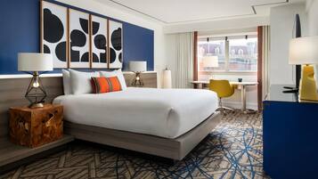 Habitación de hotel con una cama grande, lámparas de noche, una mesita de madera, un escritorio con una silla y vistas a la ciudad desde la ventana.