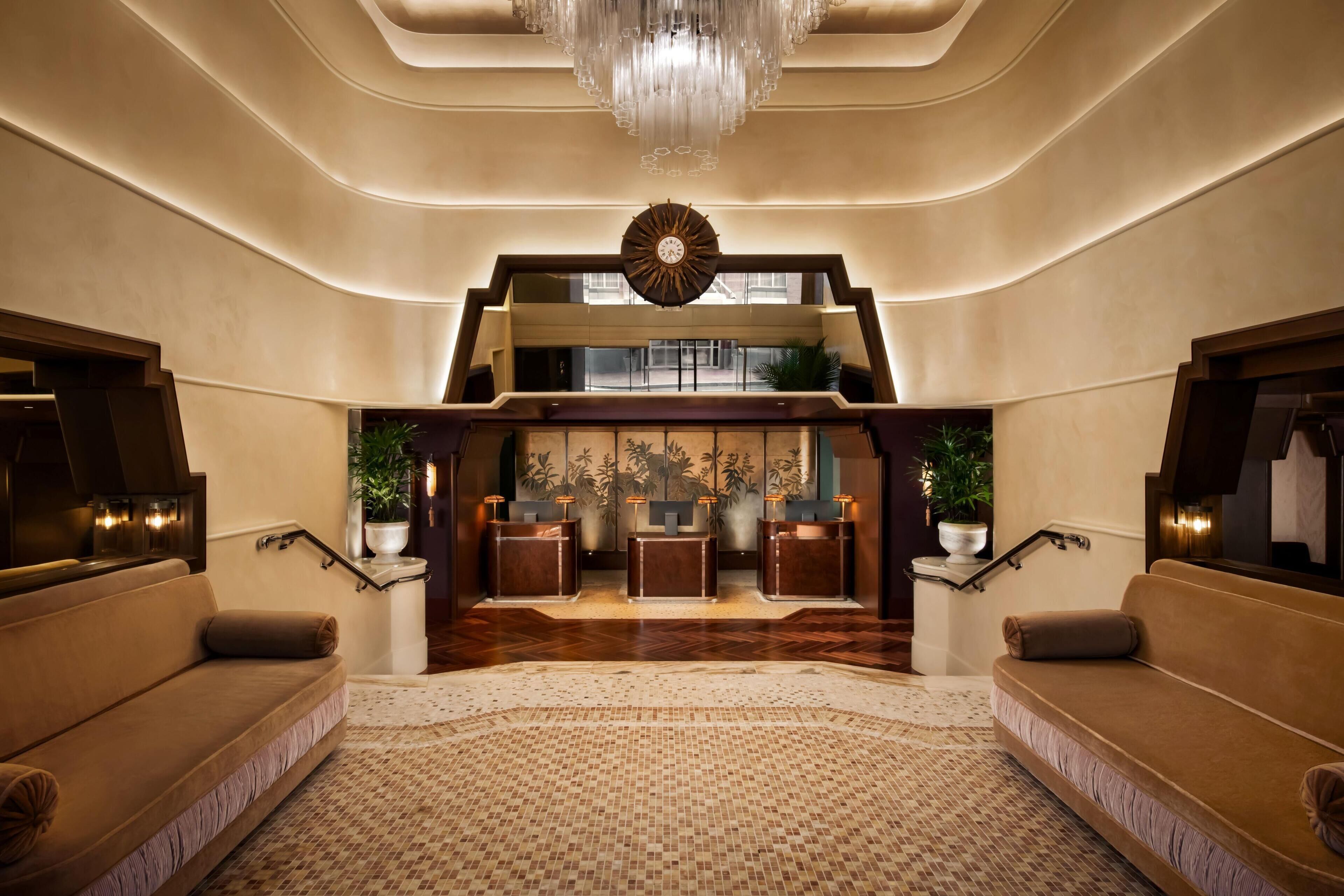 A spacious lobby with a grand staircase, a reception desk, and a chandelier.