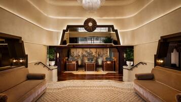 A spacious lobby with a grand staircase, a reception desk, and a chandelier.