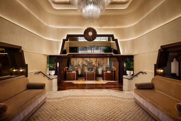 A spacious lobby with a grand staircase, a reception desk, and a chandelier.