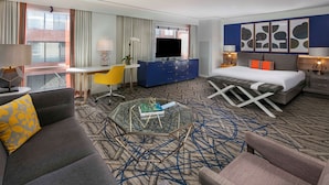 A hotel room with a bed, a desk, a sofa, a coffee table, and a TV.