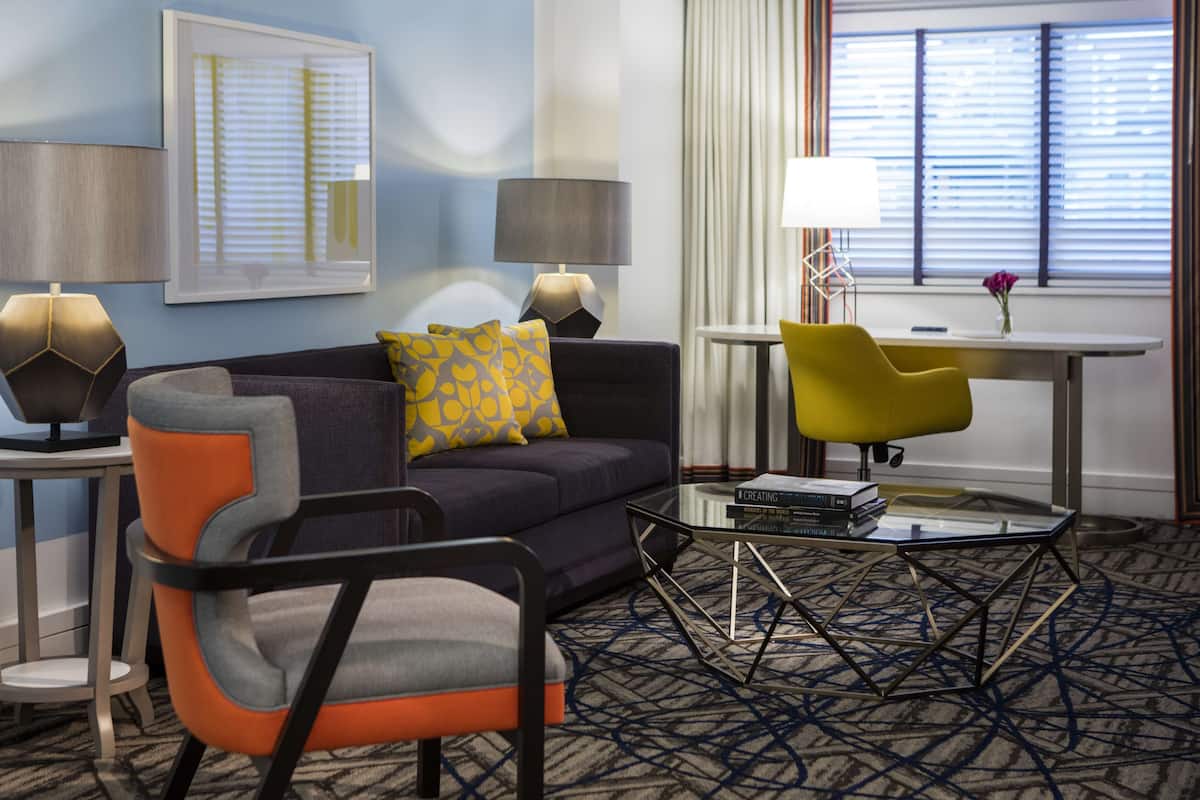 A modern hotel room with a sofa, armchair, and a small table with books.