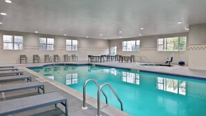 Une piscine intérieure à l’eau d’un bleu cristallin, entourée de chaises longues et de tables, et dotée de grandes fenêtres sur toute la longueur des murs.