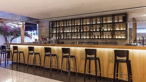 Een bar met een lange toonbank, meerdere krukken en een goed gevulde flessenkast.