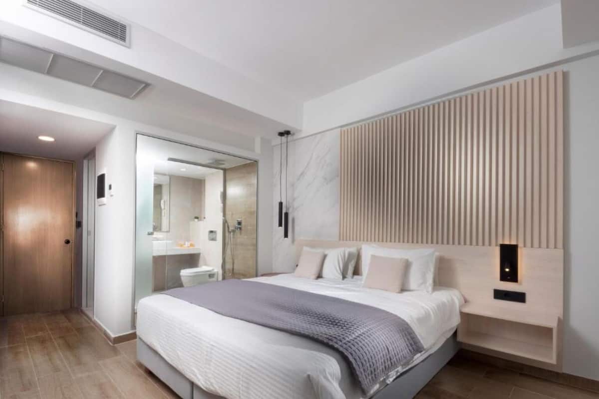 Une chambre moderne avec un grand lit, une tête de lit en bois, une table de chevet intégrée et une cabine de douche en verre.