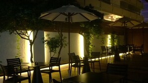 Een terras met tafels, stoelen, parasols en planten.