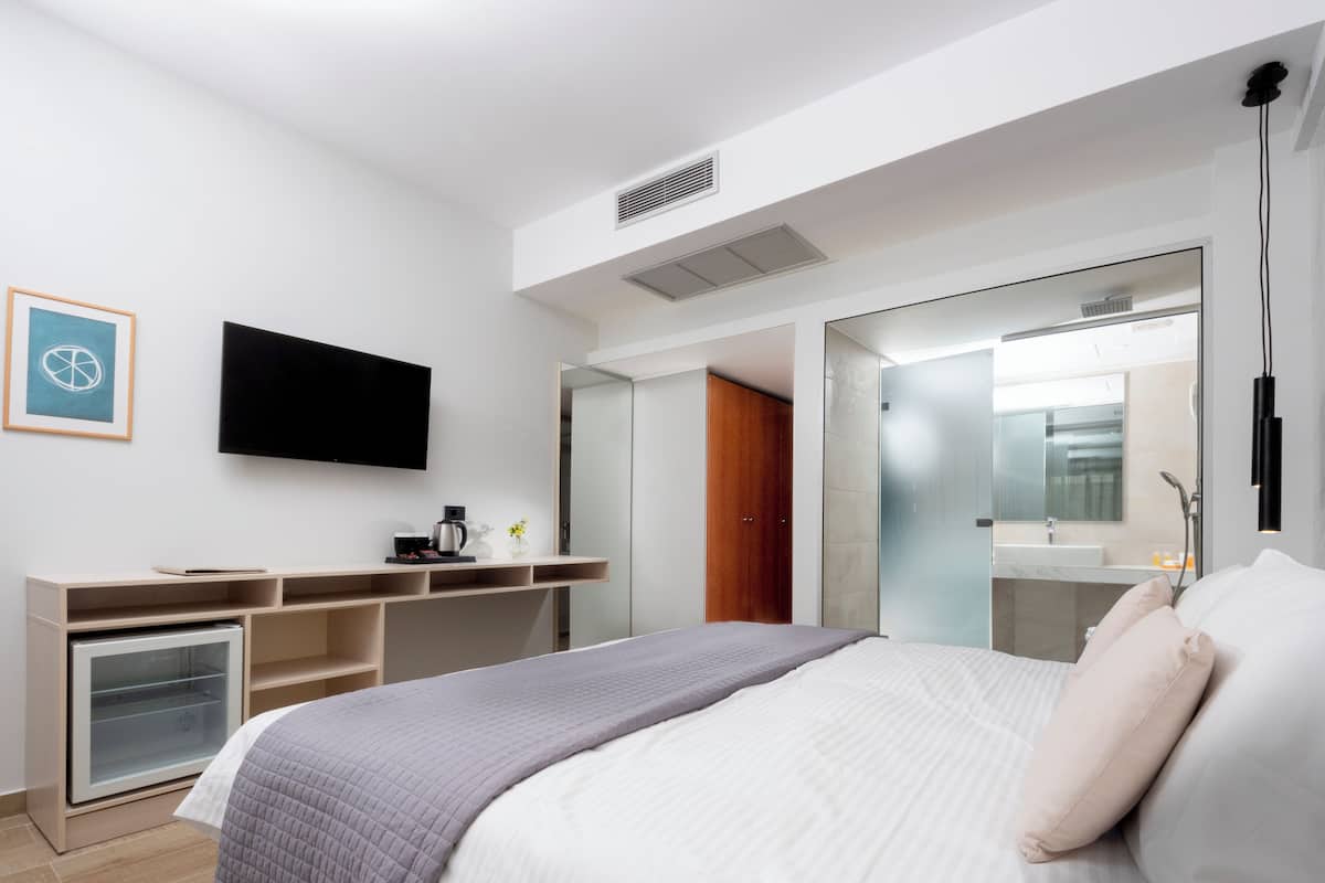 Une chambre d’hôtel moderne équipée d’un lit, d’une télévision à écran plat, d’un bureau avec une machine à café et d’un dressing.