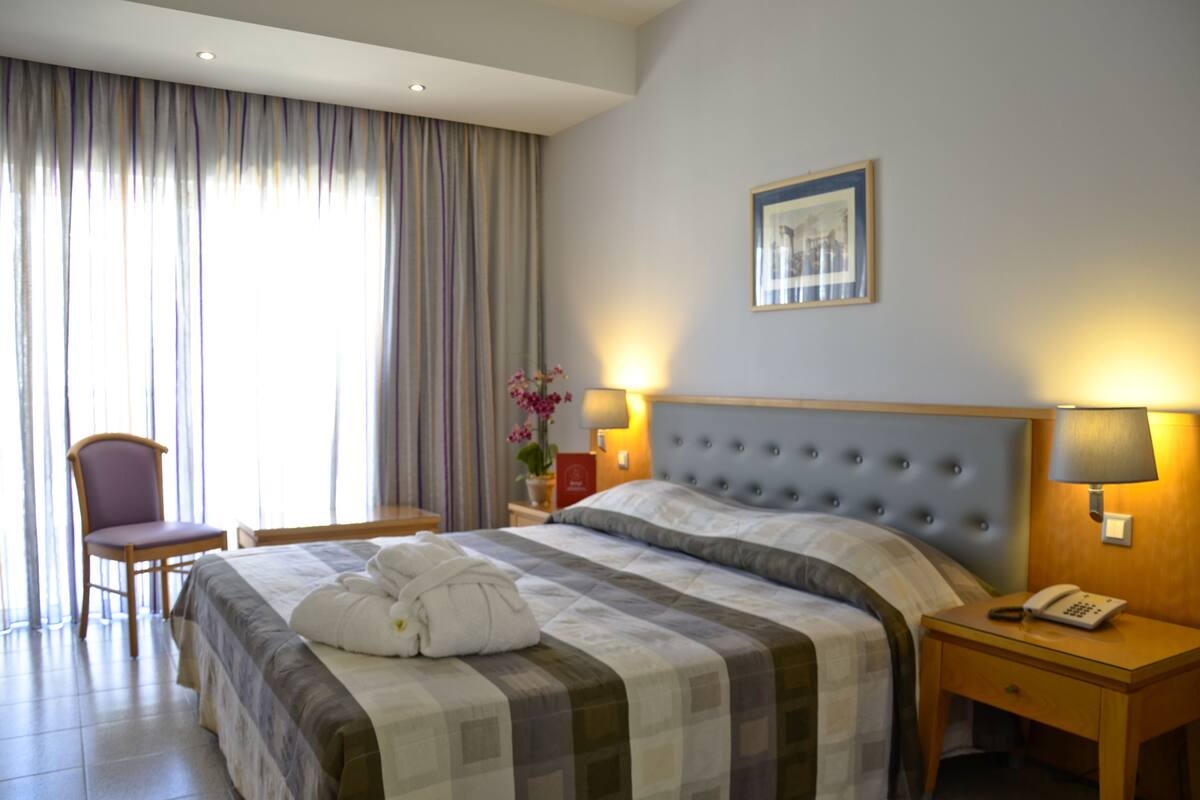 Une chambre d’hôtel avec un lit, une chaise, une table de chevet avec une lampe et un tableau au mur.