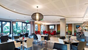 Un restaurante moderno con mesas redondas, sillas negras y blancas, y una lámpara colgante grande.