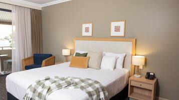 A hotel room with a large bed, two pillows, a nightstand with a lamp and phone, a chair, and two framed pictures on the wall.