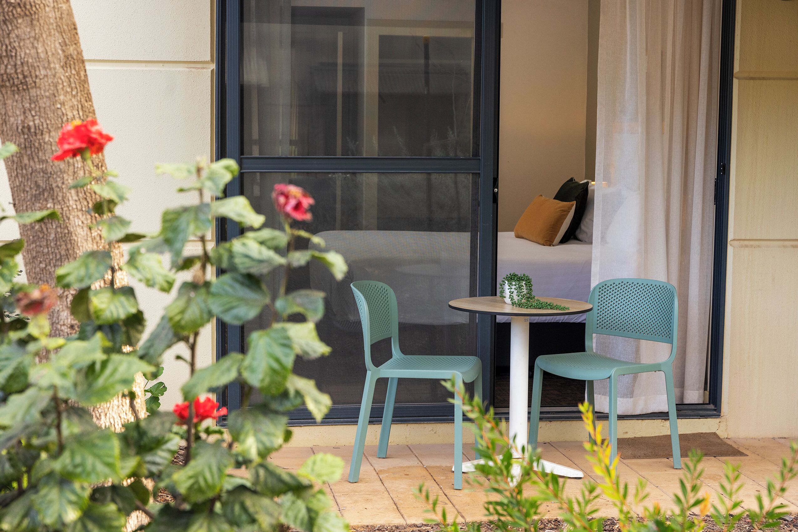A small patio area with two chairs and a table, a sliding glass door, and a view of a building.