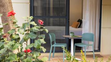 A small patio area with two chairs and a table, a sliding glass door, and a view of a building.