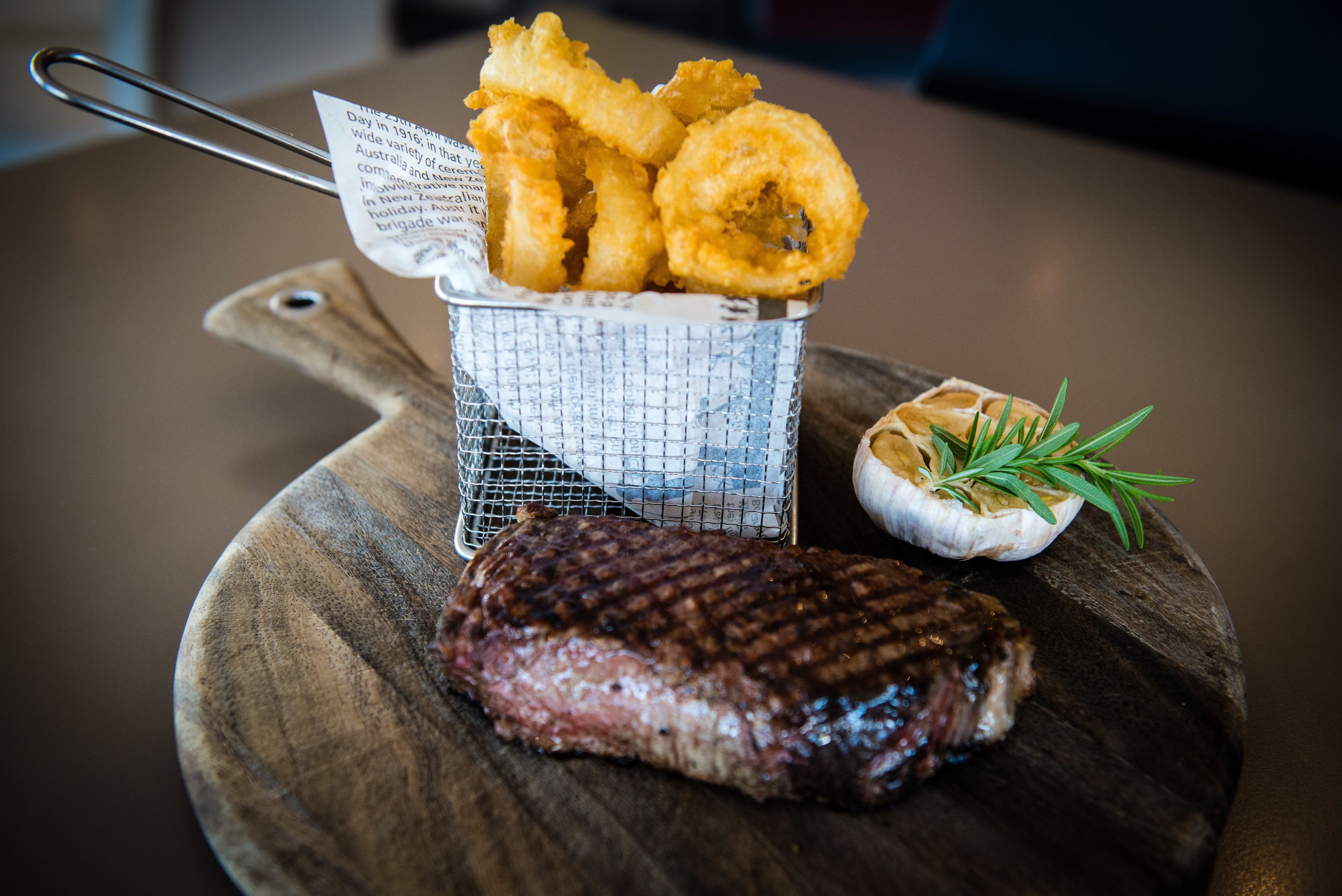 A grilled steak with onion rings and a garlic clove on a wooden board.