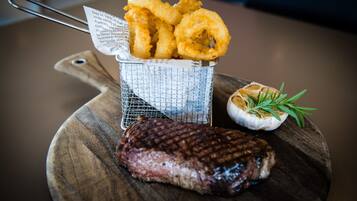 A grilled steak with onion rings and a garlic clove on a wooden board.
