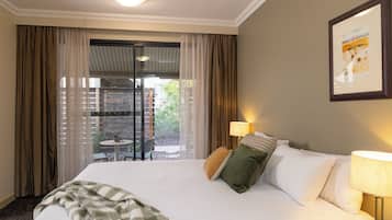 Ein Hotelzimmer mit einem großen Bett, Blick ins Freie durch eine Schiebetür und einem kleinen Tisch mit Stuhl draußen.