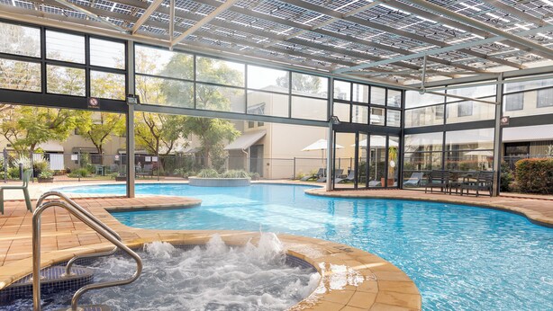 Piscina con jacuzzi, rodeada por una zona cubierta con paredes de cristal y techo.