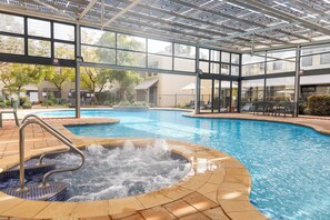 Piscina con jacuzzi, rodeada por una zona cubierta con paredes de cristal y techo.