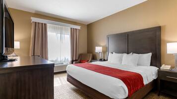 A hotel room with a large bed, a desk, a chair, and a TV.