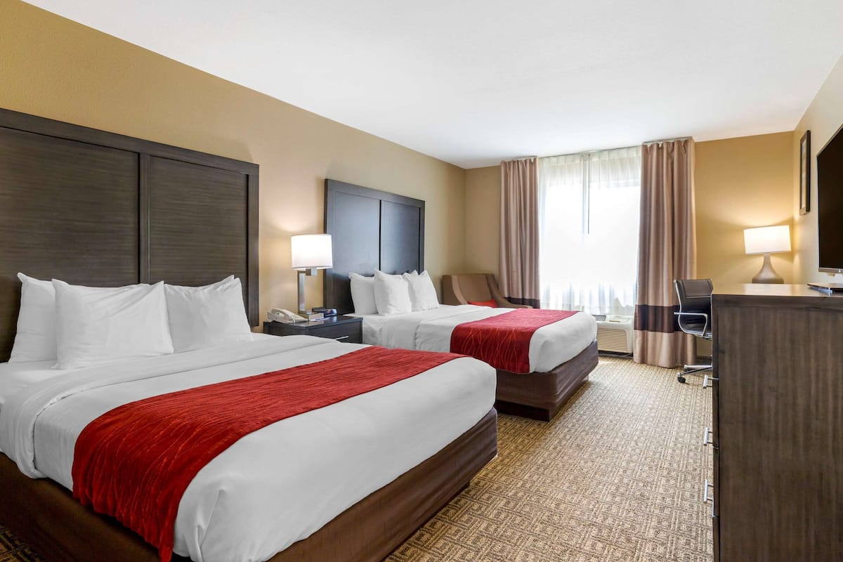 A hotel room with two beds, a desk, a chair, and a TV.