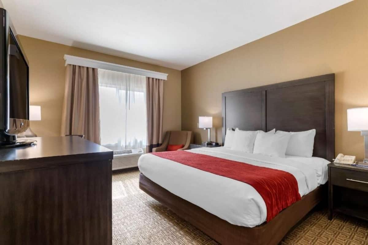 A hotel room with a large bed, a desk, a chair, and a television.