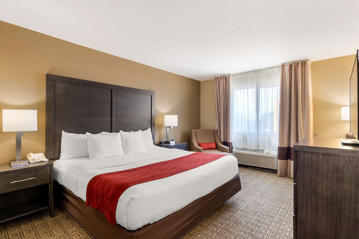 A hotel room with a large bed, two bedside tables with lamps, a chair, a desk, and a window with curtains.