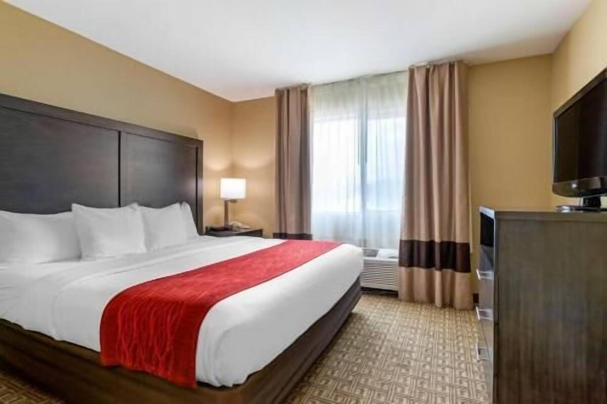 A hotel room with a large bed, a desk with a lamp, a television, and a window with curtains.