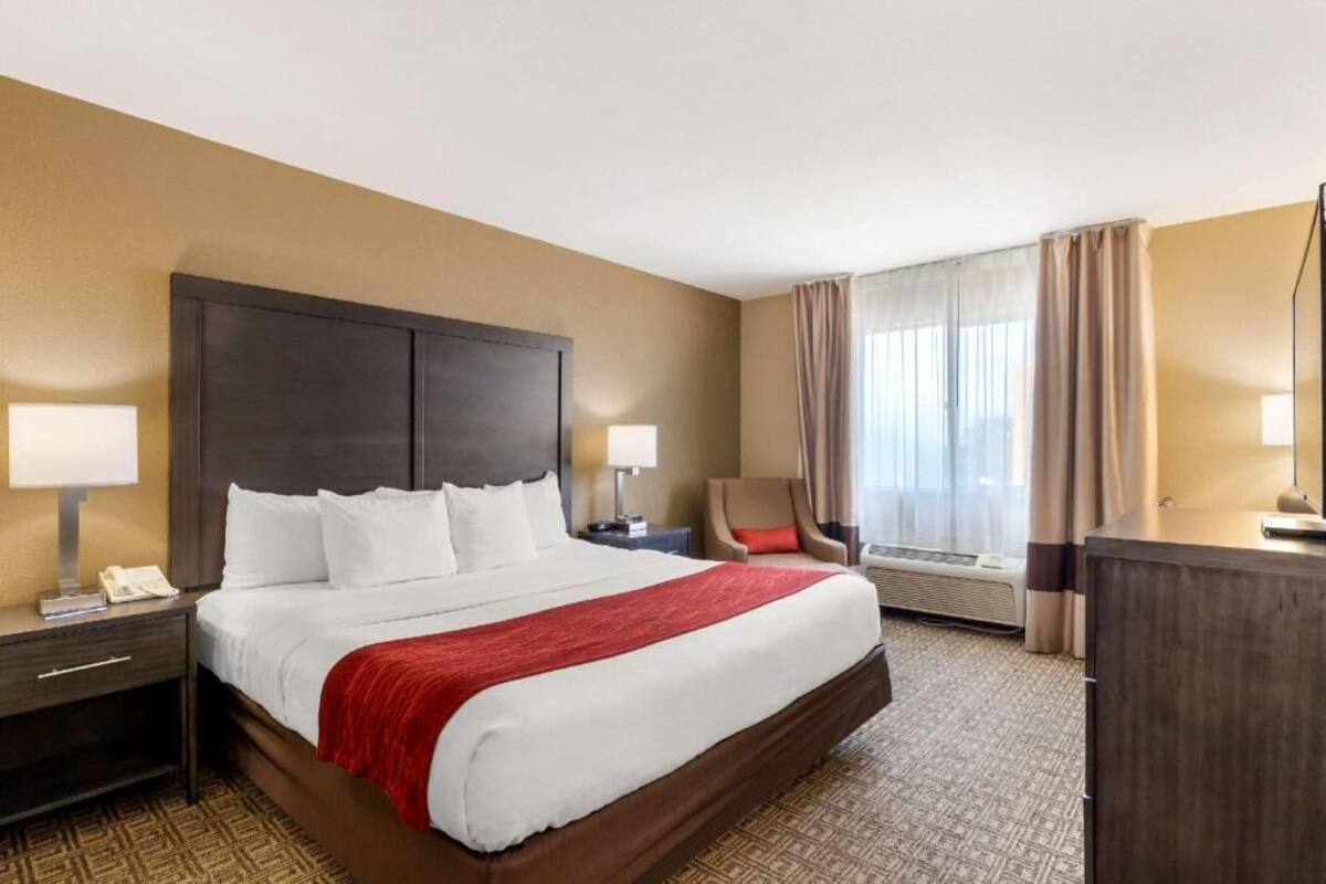 A hotel room with a large bed, two bedside tables, a chair, a desk, and a window with curtains.